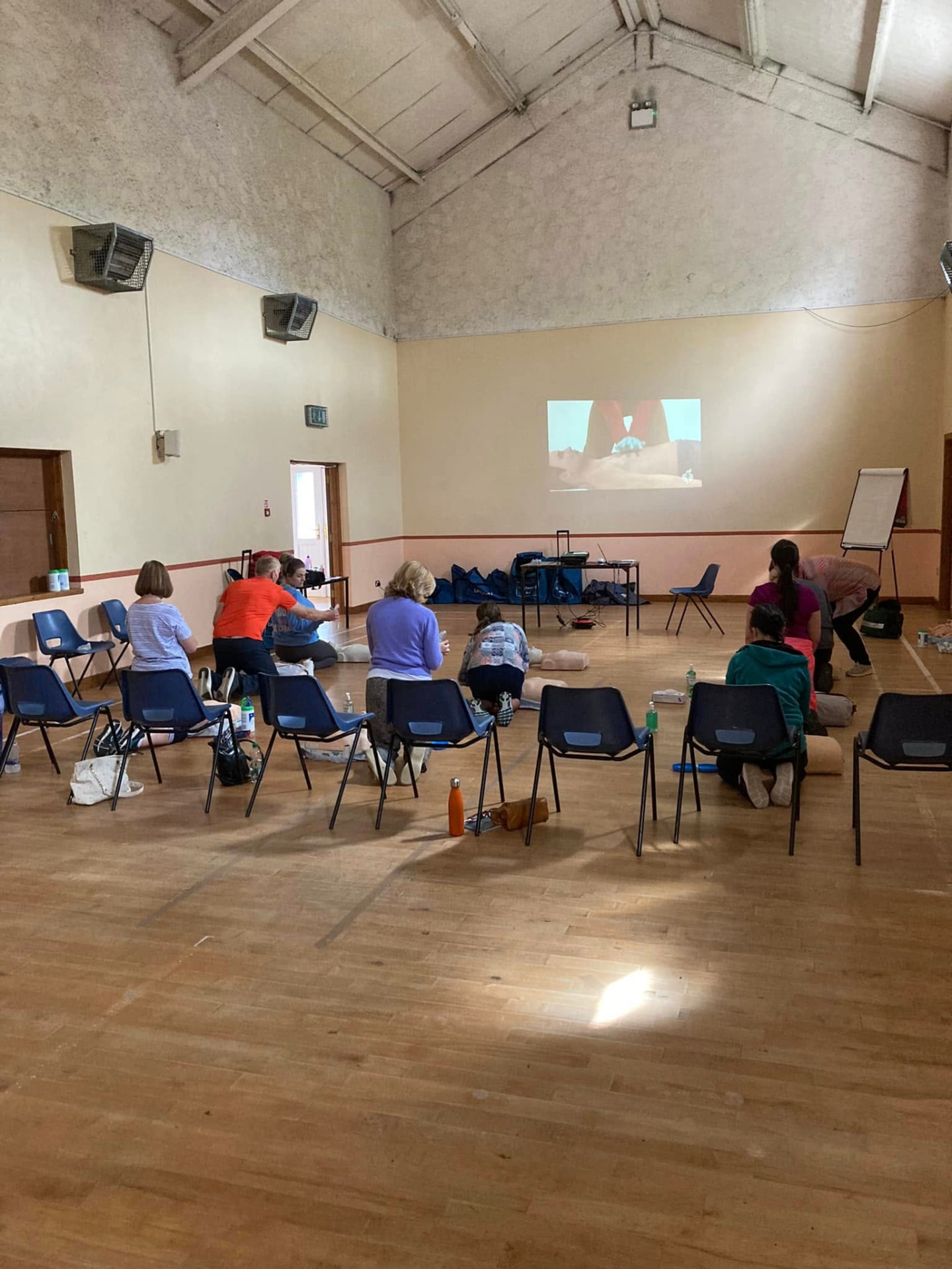 Participants kneeling beside training manikins during a CPR practice session in a community hall